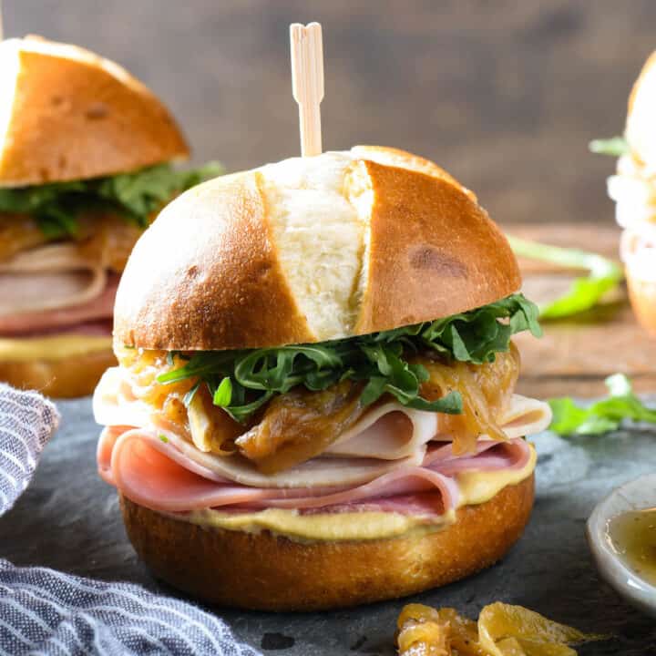 A ham and turkey slider made on a pretzel roll, dressed with arugula, caramelized onions and mustard.
