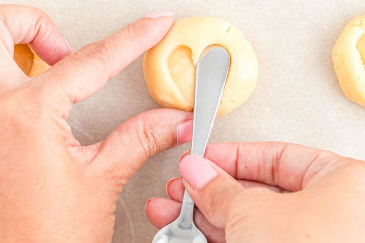 A woman's hands using a small spoon to press a heart shape into a round of cookie dough.