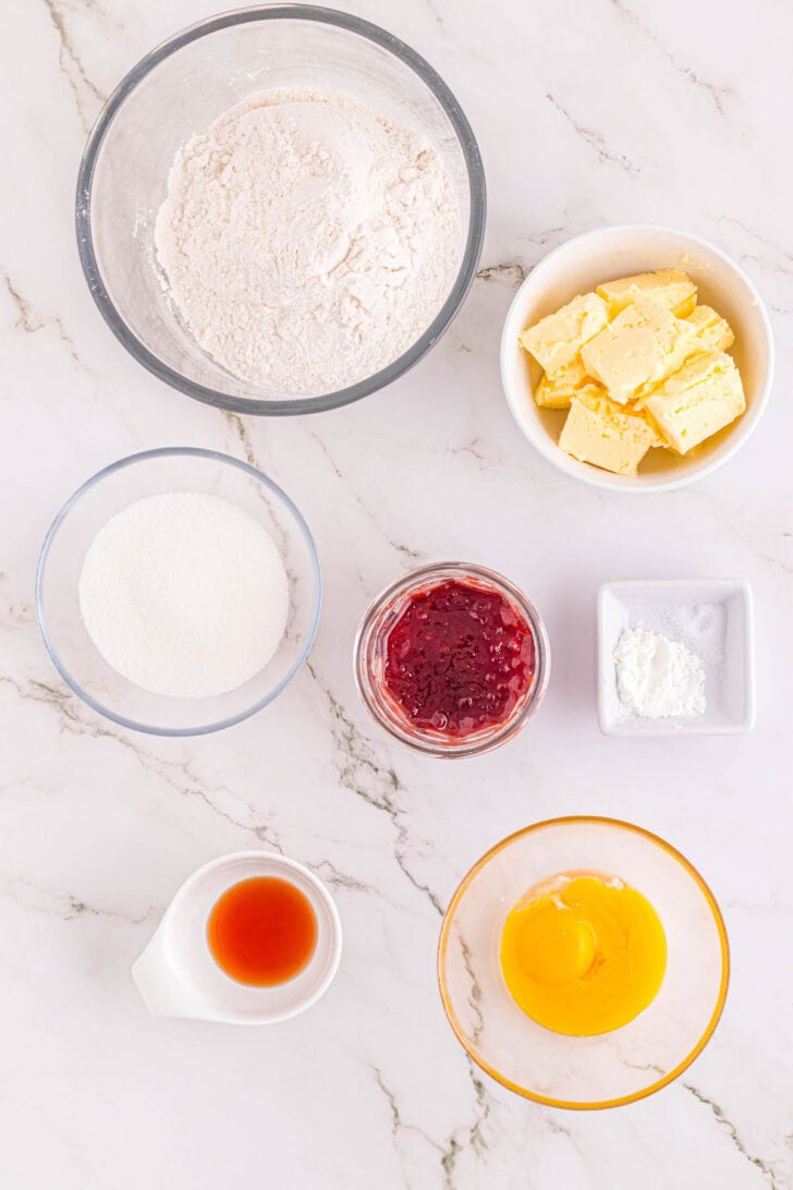 Ingredients needed for heart cookies, in bowls on a light surface.