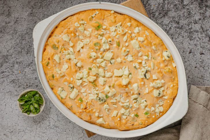 Greek yogurt buffalo chicken dip in a baking dish, topped with blue cheese and green onions.