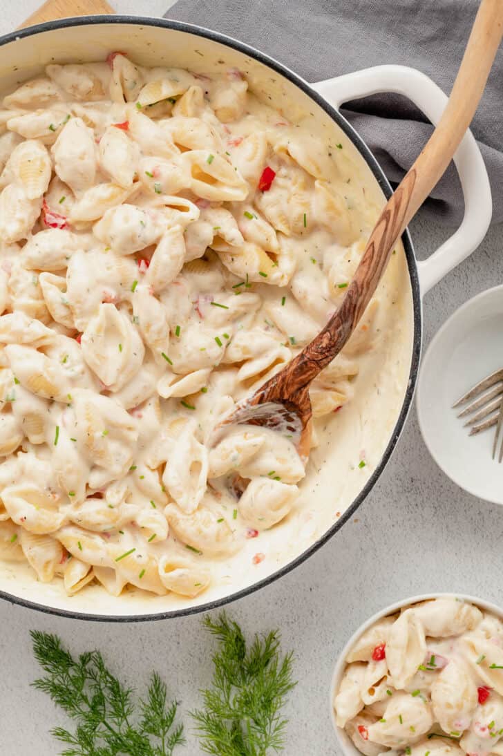 A white Dutch oven filled with pimento mac and cheese, with a wooden spoon stirring it.