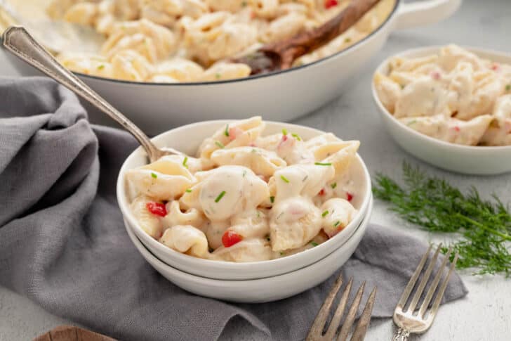 A small white bowl filled with pimento cheese mac and cheese, with a spoon scooping into it.