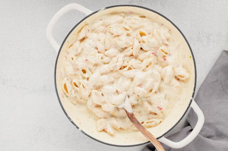 A white Dutch oven filled with pimento cheese mac and cheese, with a wooden spoon stirring it.