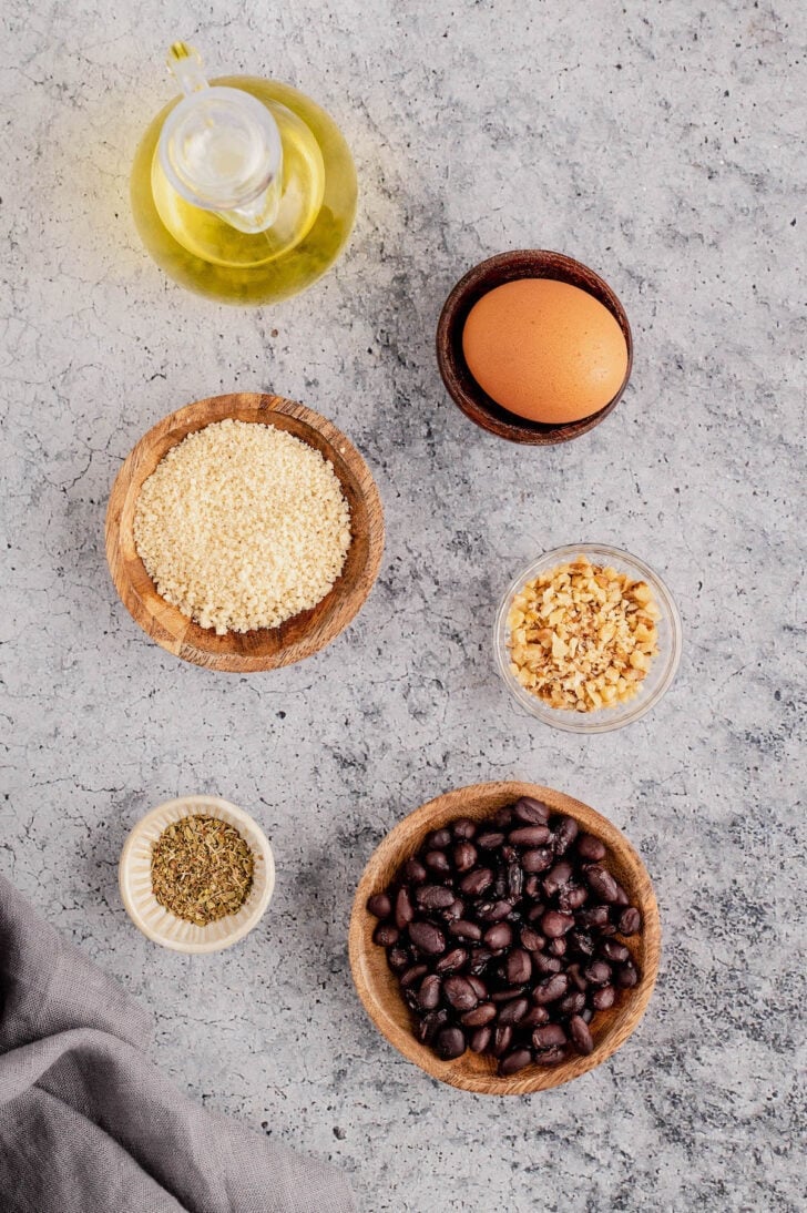 Ingredients on a rustic surface, including beans, cheese, breadcrumbs, and egg and spices.