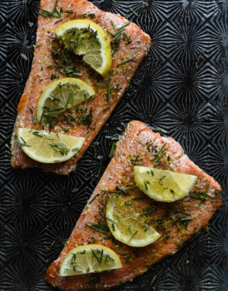 Baked sockeye salmon covered in herbs and lemon slices on a textured baking pan.