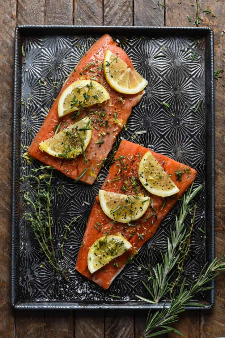 An uncooked sockeye salmon recipe, with fish topped with lemon slices and herbs on a textured baking pan.