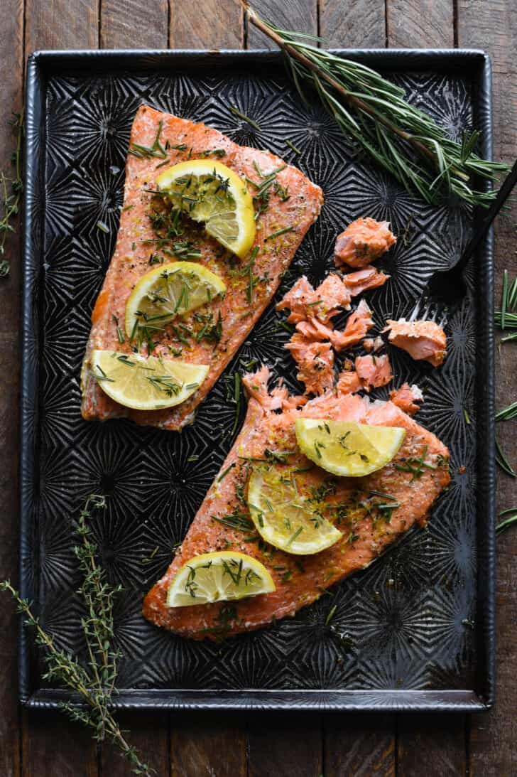 Cooked pink fish being flaked with a fork on a textured baking pan.