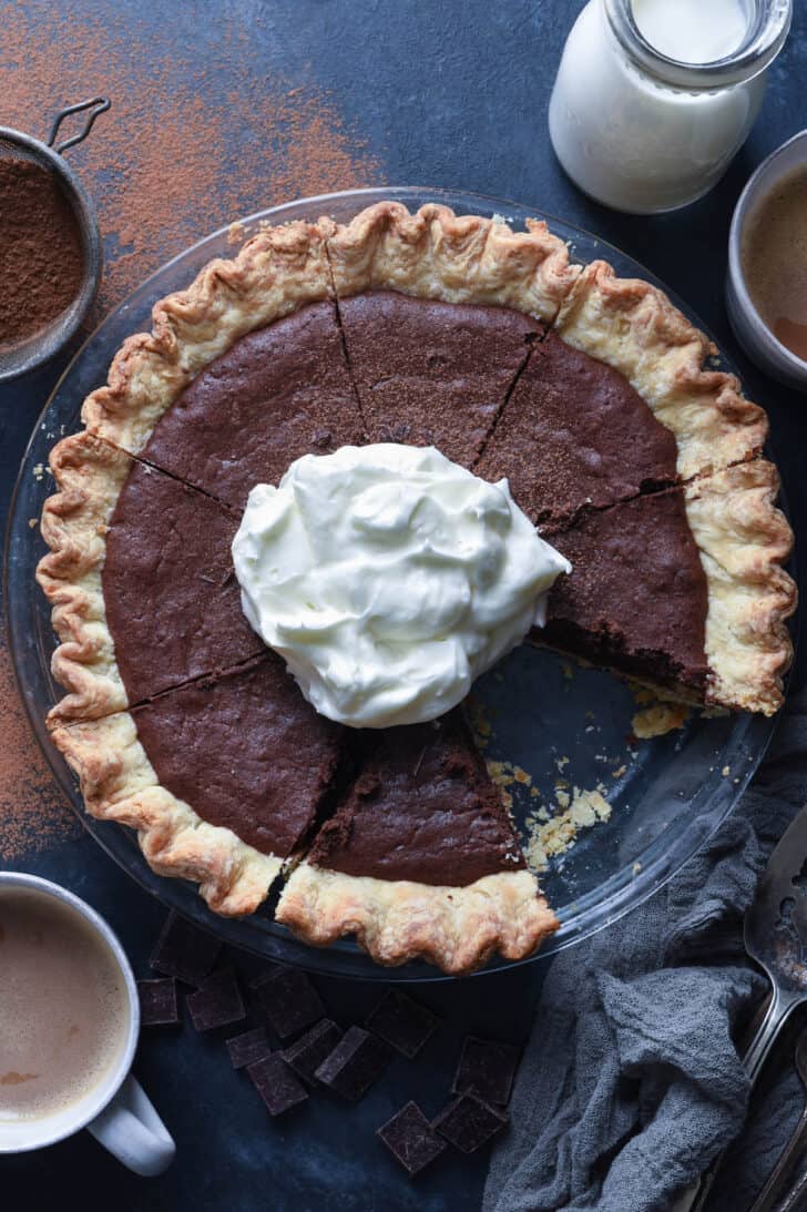 A brownie pie topped with whipped cream with once piece taken out of it.