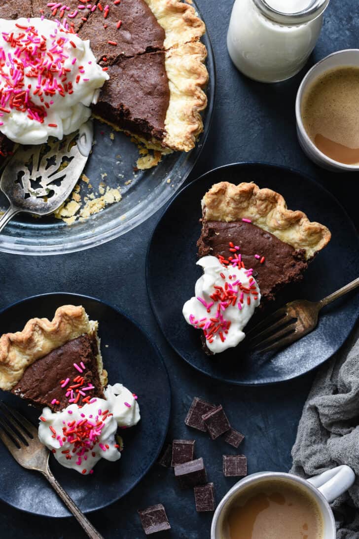 Two pieces of chocolate tart on dark plates, topped with whipped cream and pink and red sprinkles.