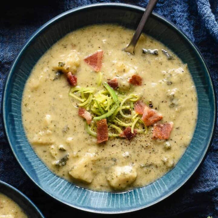 A blue bowl filled with Irish colcannon soup, garnished with sliced leeks and bacon.