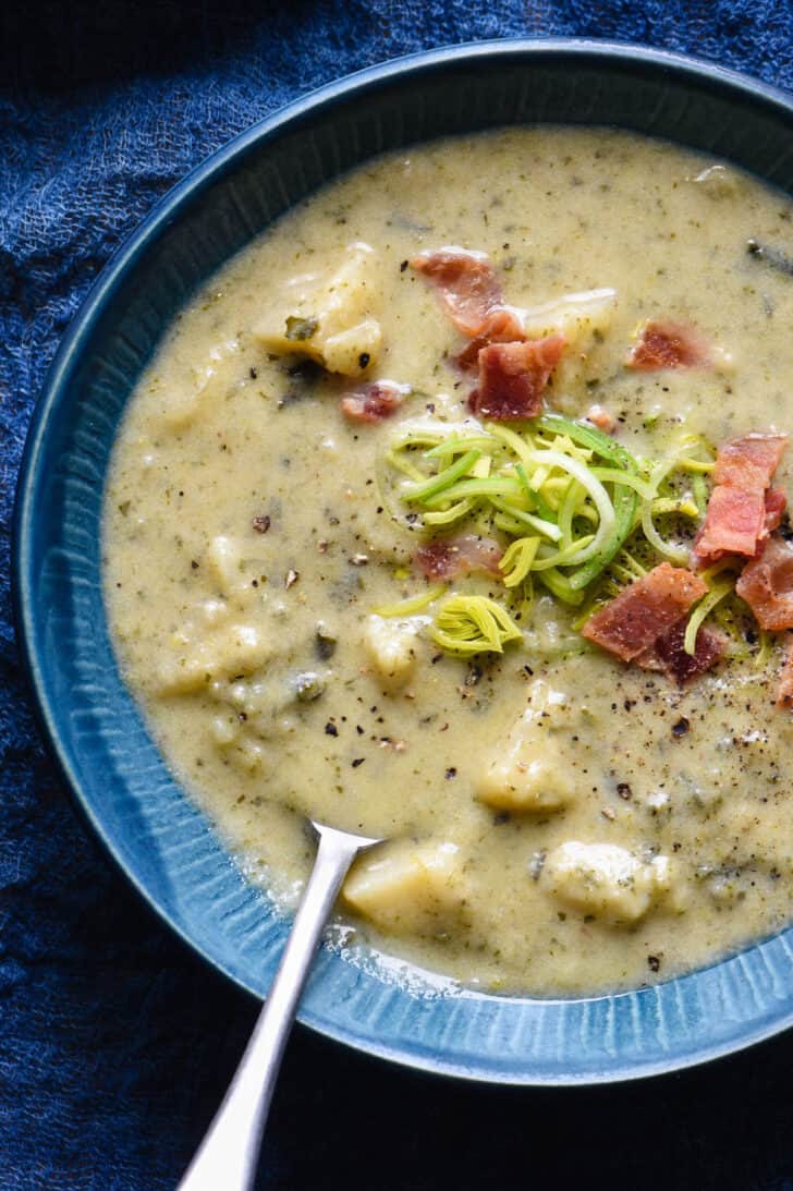 A blue bowl filled with Irish colcannon soup, garnished with sliced leeks and bacon.