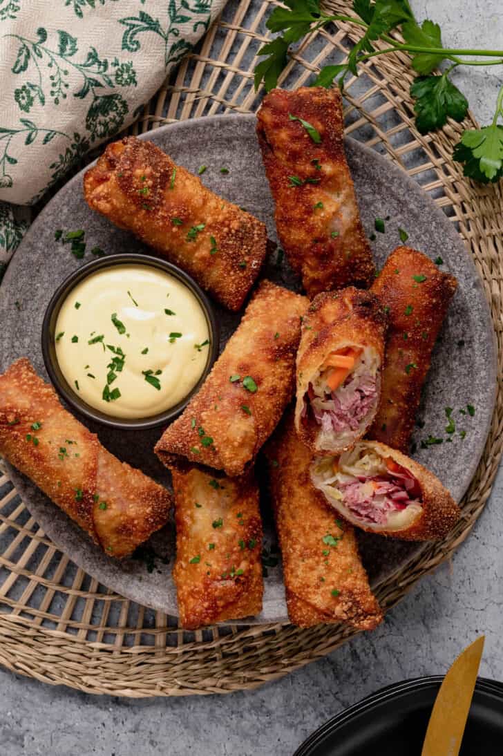 Corned beef egg rolls and creamy mustard dipping sauce on a gray speckled plate.