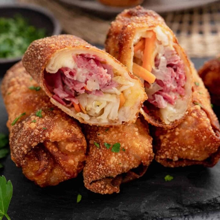 A plate of corned beef egg rolls. One egg roll is cut in half, showing the inside filling.