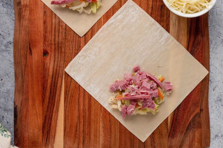 An egg roll wrapper on a wooden cutting board with a dollop of coleslaw and corned beef on it.