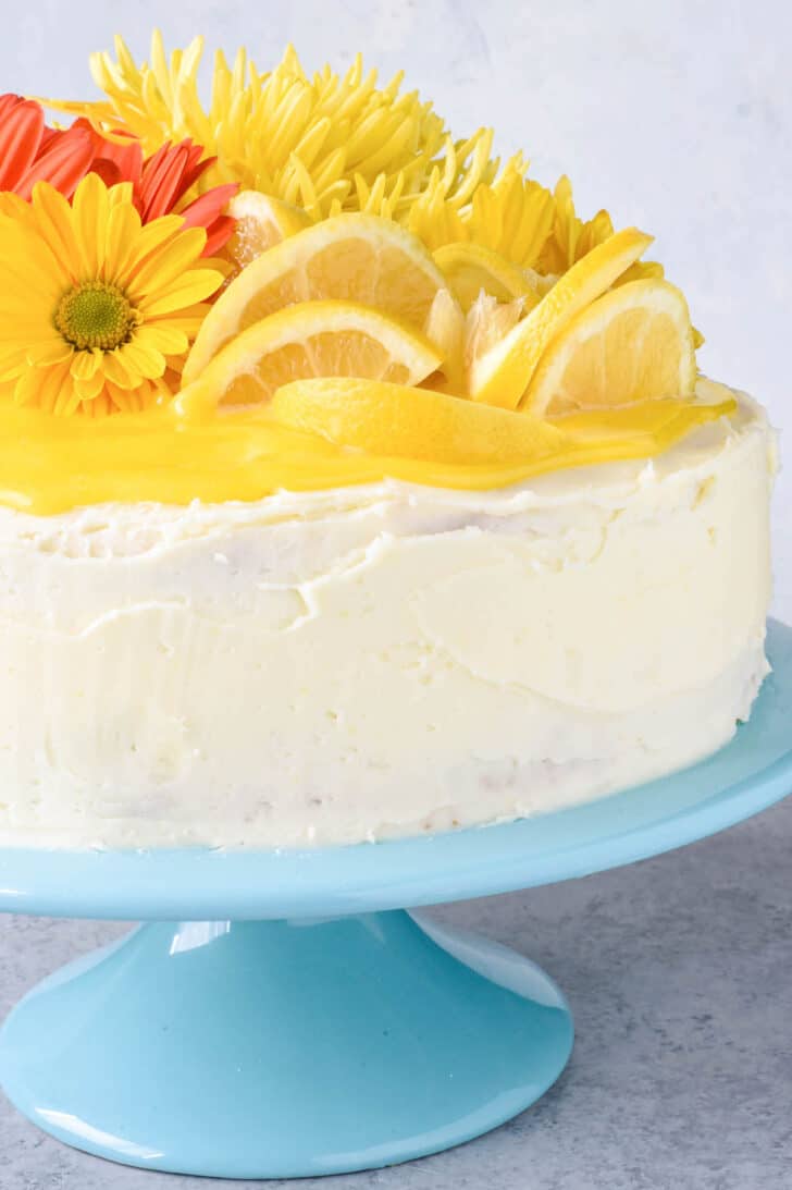 A cake decorated with white frosting, citrus wedges and yellow and orange flowers, on a light blue cake stand.