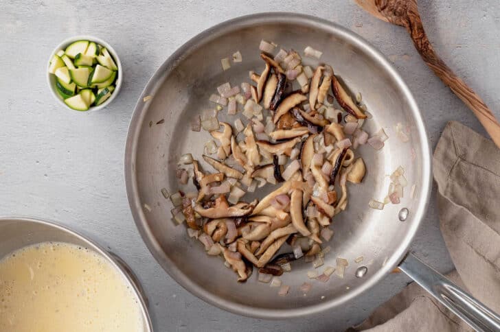 Mushrooms and shallots being sauteed in a stainless steel skillet for a quiche recipe vegetarian.