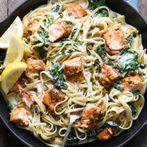 A large blue cast iron skillet filled with creamy salmon pasta with spinach, and lemon wedges as garnish.