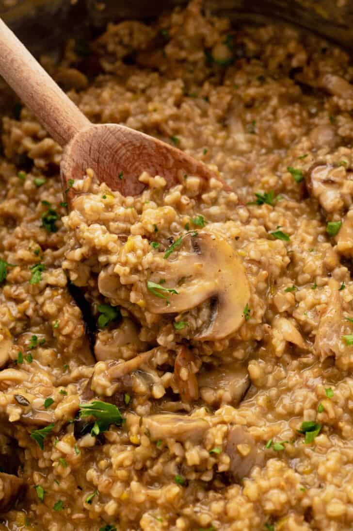 A wooden spoon digging into savory oatmeal made with steel cut oats and mushrooms.
