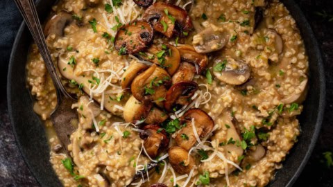 A dark shallow bowl filled with savory oatmeal topped with mushrooms, herbs and Parmesan cheese.
