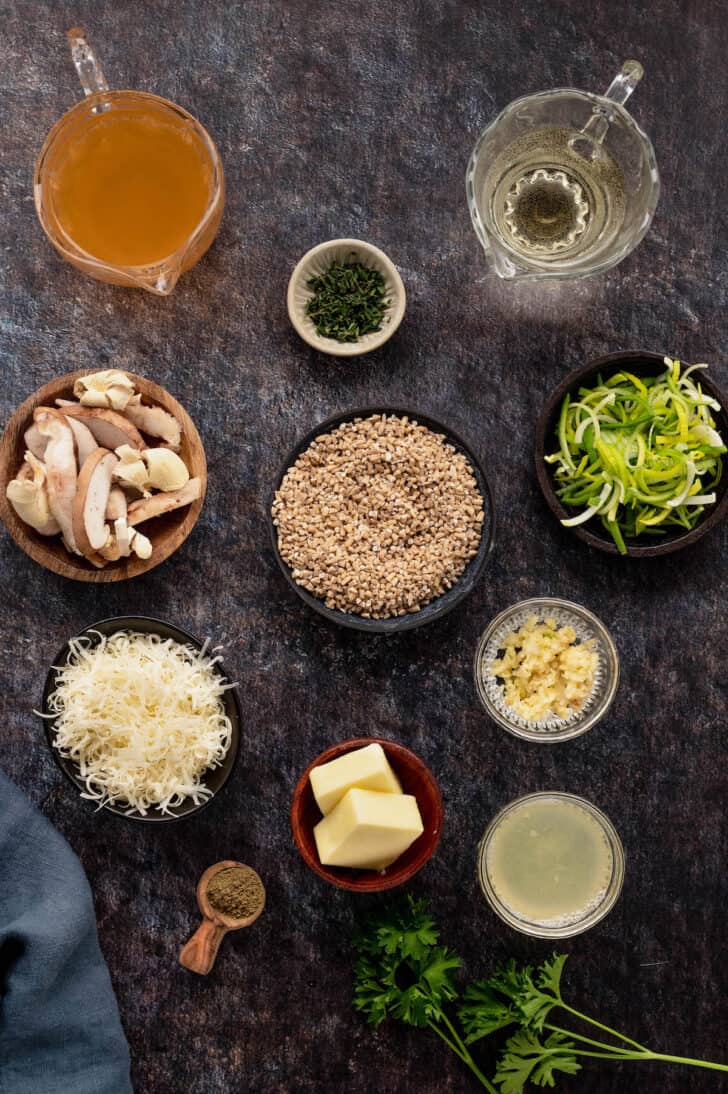 The ingredients needed for oatmeal for dinner laid out on a dark surface, including steel cut oats, mushrooms, leeks, herbs, wine, broth, cheese and butter.