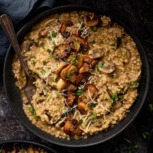 A dark shallow bowl filled with savory oatmeal topped with mushrooms, herbs and Parmesan cheese.