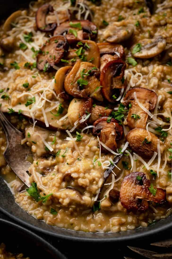 A fork digging into oatmeal risotto topped with mushrooms and cheese.