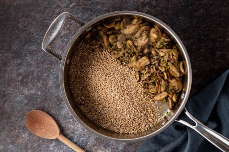 Skillet filled with cooked mushrooms and raw steel cut oats.