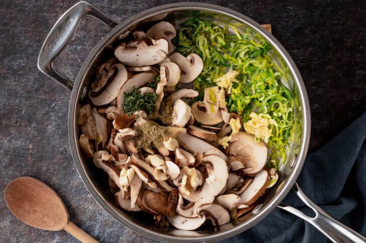 Skillet filled with sliced mushrooms and leeks, and herbs and spices.
