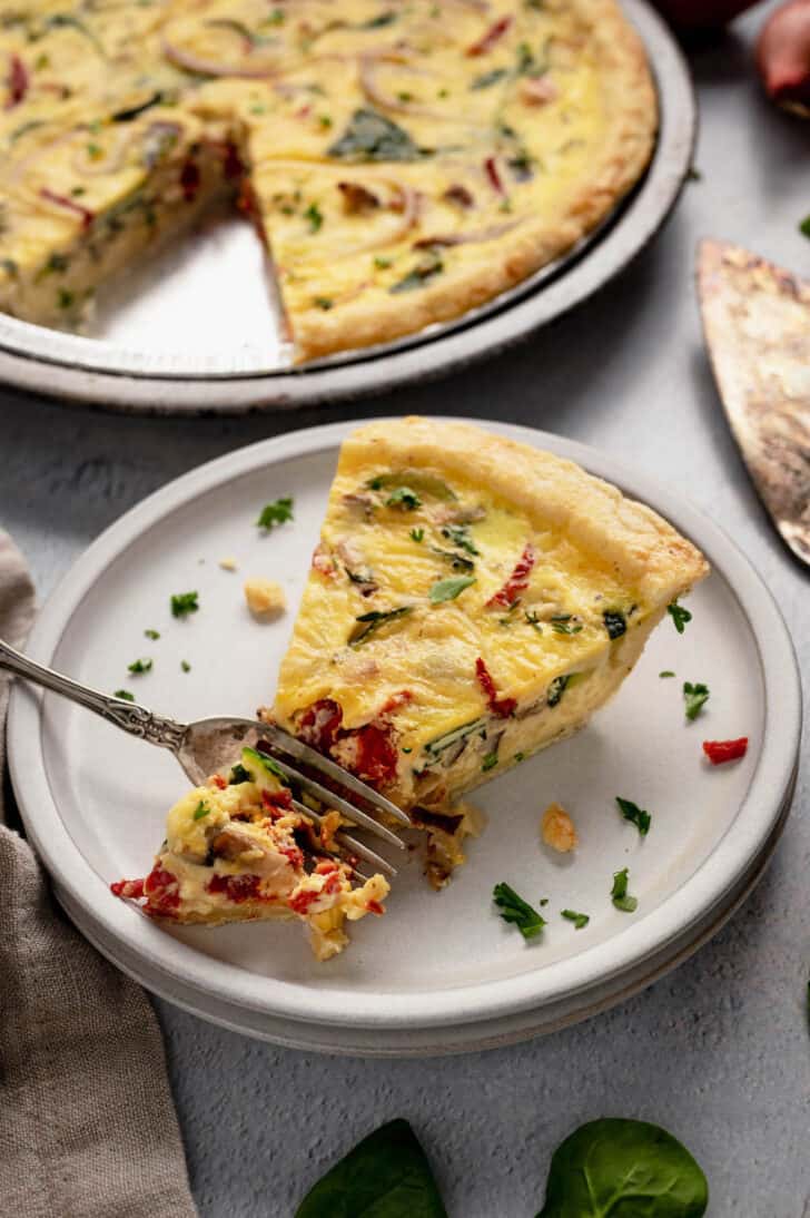 A slice of vegetarian quiche on a small white plate with a fork digging into it.