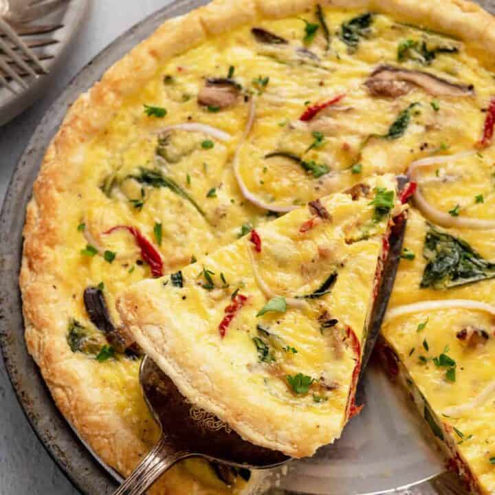 A slice of vegetarian quiche being lifted out of a full quiche in a metal pie plate.