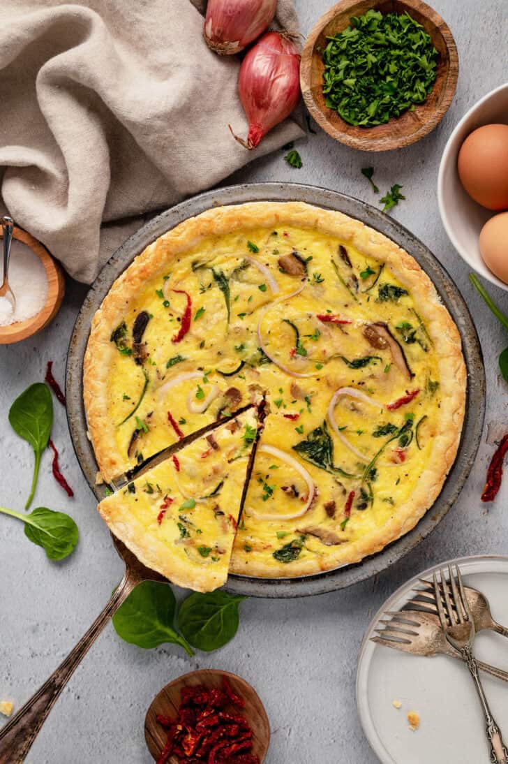 A slice of vegetarian quiche being lifted out of a full quiche in a metal pie plate.