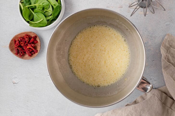 Eggs being whisked in the bowl of a stand mixer for a vegetable quiche recipe.