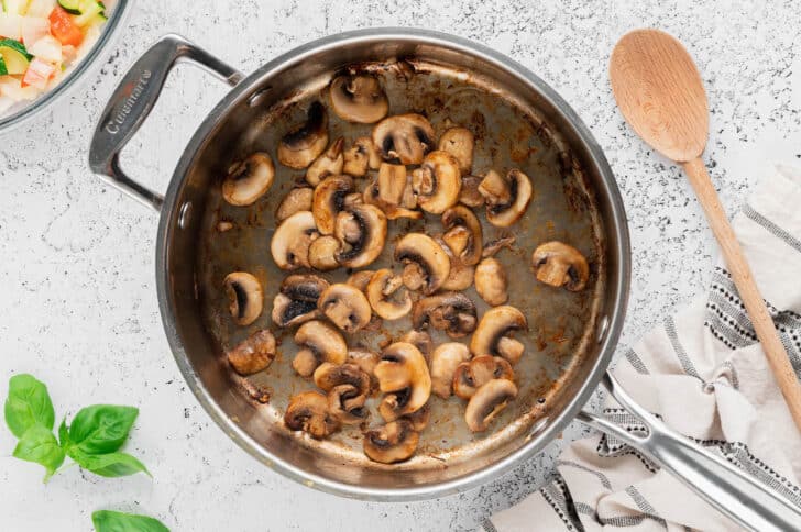 Sliced button mushrooms being sauteed in a skillet.