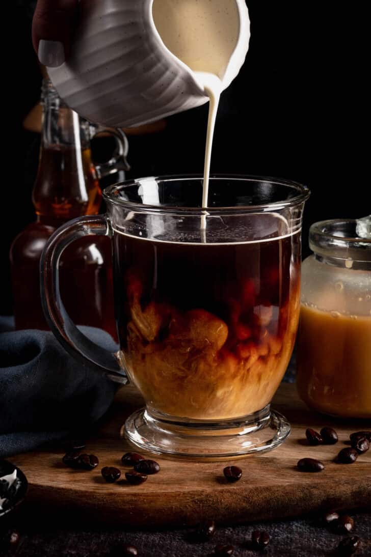 A mug of coffee with cream being poured into it.