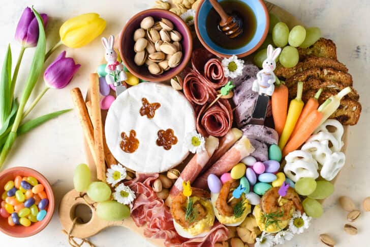 An Easter charcuterie board including cheese, meats, vegetables, candy, nuts, crackers, honey and deviled eggs.
