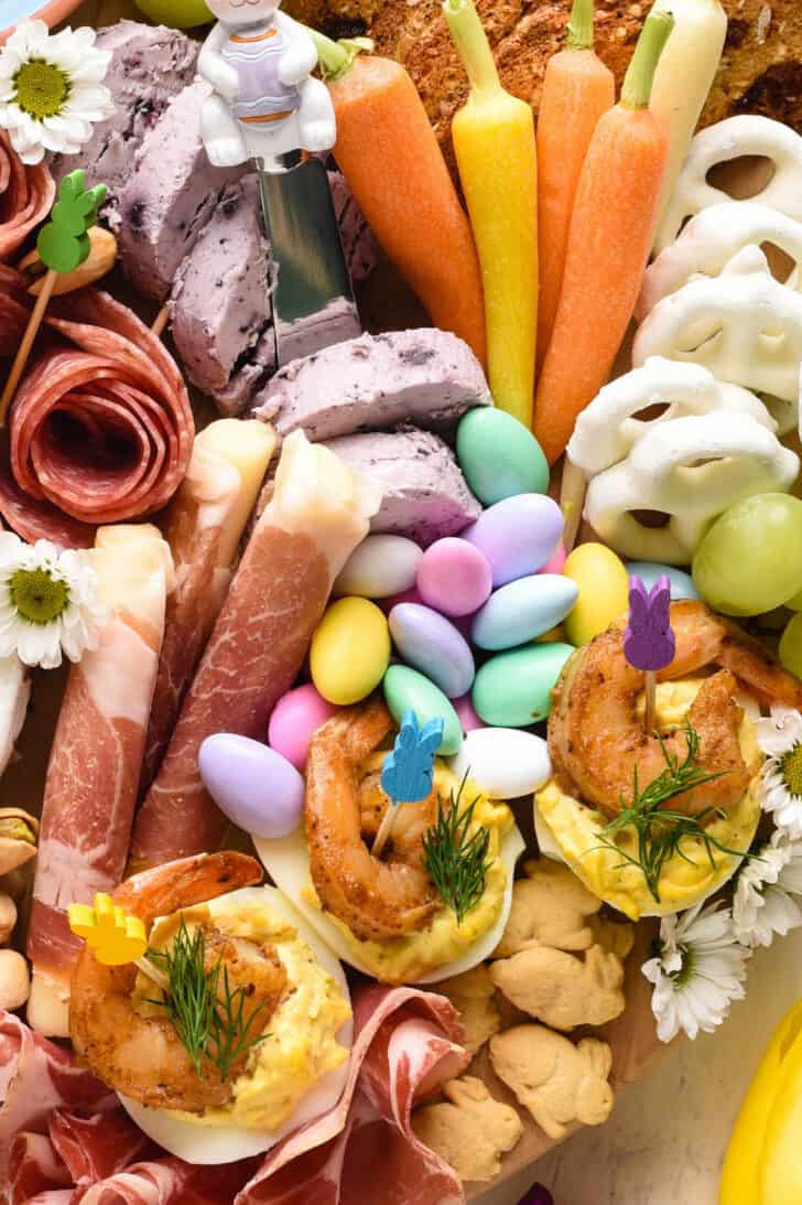 Closeup on items on an Easter charcuterie board, including deviled eggs topped with shrimp, prosciutto, grapes, bunny cookies and Jordan almonds.