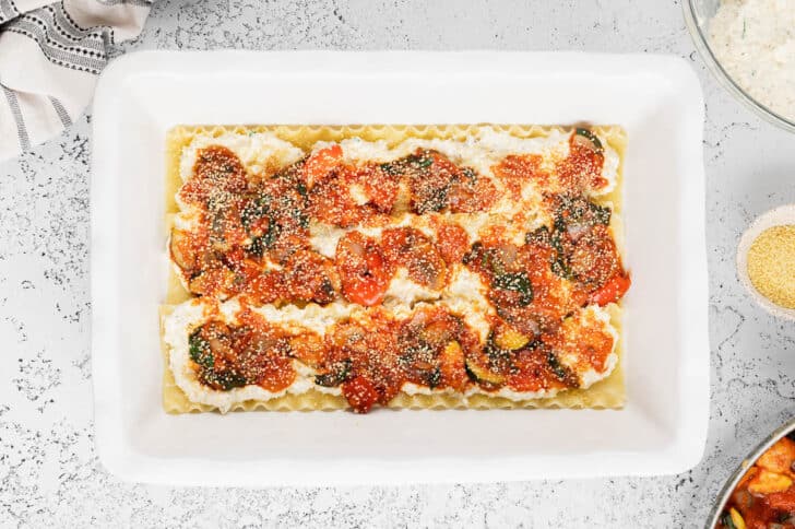 A white lasagna dish layered with lasagna noodles, a cheese mixture, a vegetable marinara mixture and dried couscous.