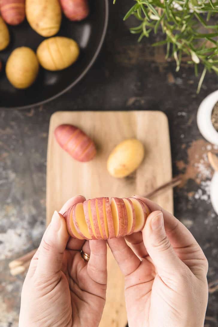 Two hands holding up a small potato that has been cut like an accordion.