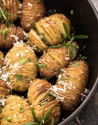 Mini Hasselback potatoes sprinkled with rosemary in a cast iron skillet.