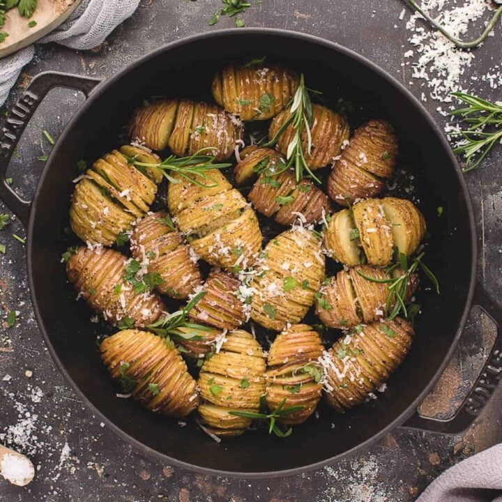 Mini Hasselback potatoes in a cast iron skillet, sprinkled with rosemary sprigs and shredded Parmesan cheese.