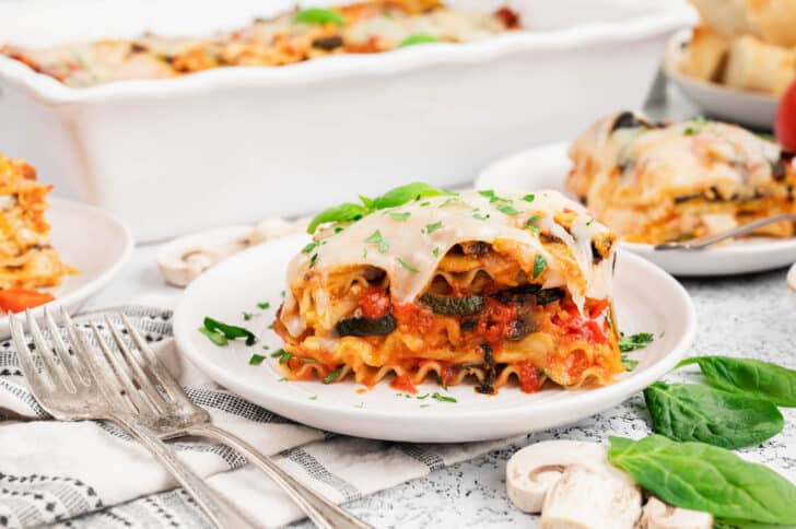 A slice of veggie lasagna garnished with green herbs on a small white plate.