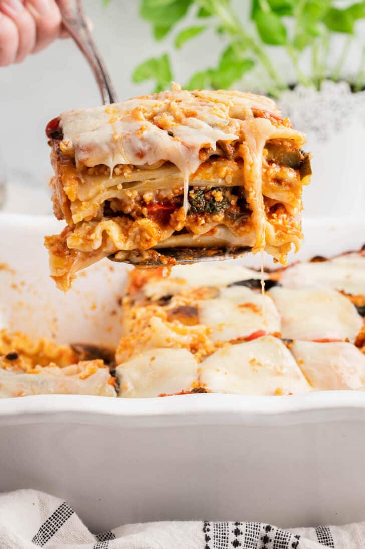 A piece of vegetables lasagna being lifted out of a white baking dish.