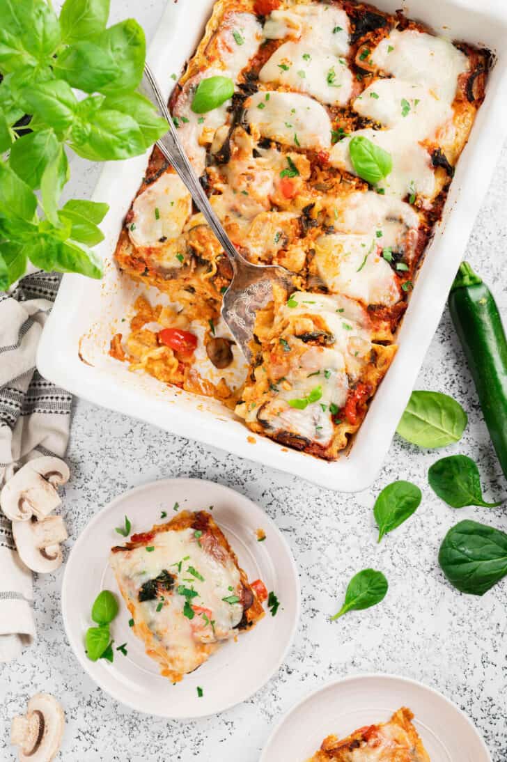 A white baking dish of pasta casserole, with a serving utensil about to lift one piece out.