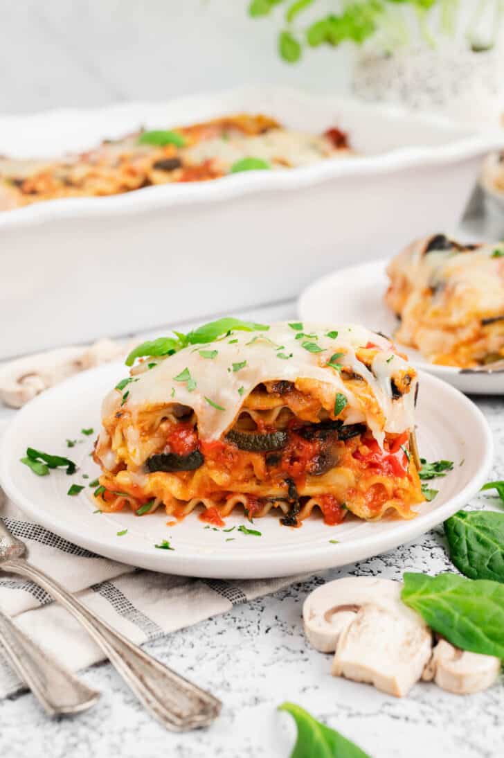 A slice of the best veggie lasagna recipe garnished with green herbs on a small white plate.