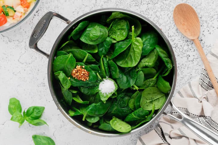 Fresh spinach, salt and red pepper flakes in a skillet.