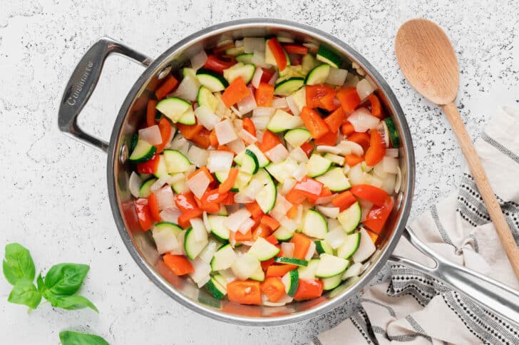 Vegetables like zucchini, red pepper and onion being sauteed in a skillet.