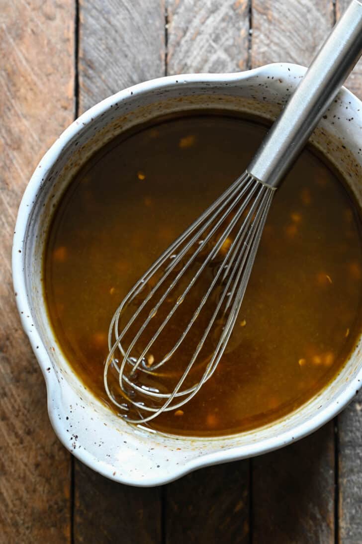 A speckled bowl filled with a brown sauce mixture, with a metal whisk in it.