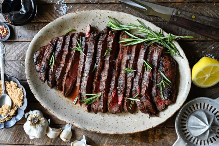 A cooked, sliced flank steak on a speckled platter, with rosemary garnishing the steak.