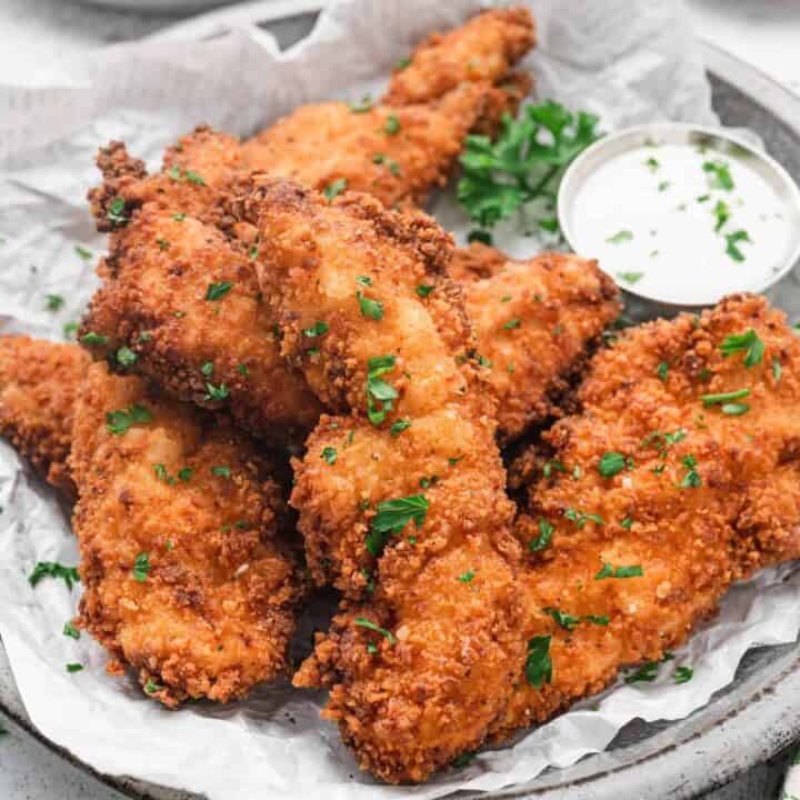 Fried buttermilk chicken tenders on a parchment-lined plate with a side of ranch dressing, sprinkled with parsley.