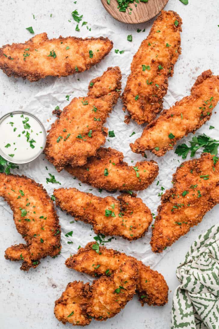 Buttermilk chicken tenders, sprinkled with parsley, on crumpled white paper.